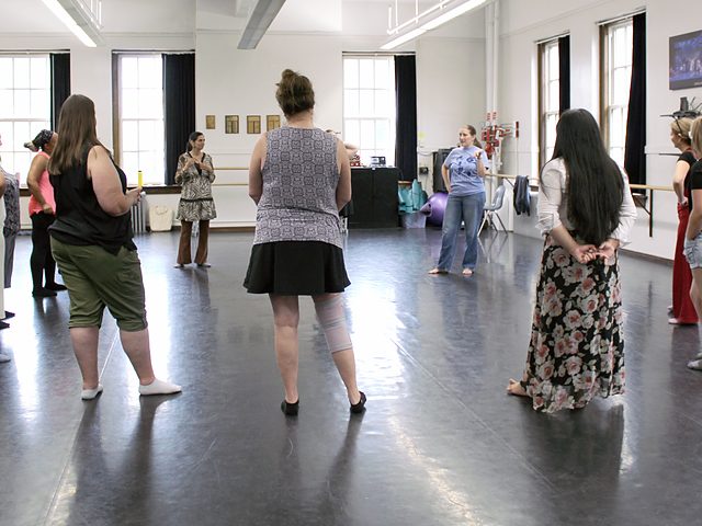 Educators standing in a circle in a studio while Lainie Hodges leads an exercise.