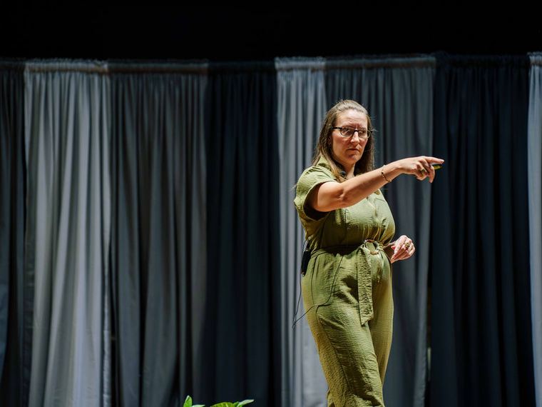 Lainie Hodges presenting on stage, gesturing to an audience.