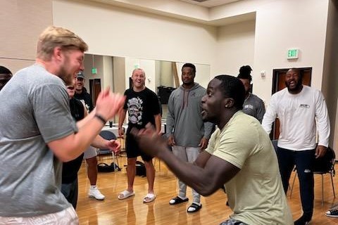 Two players facing each other mid-exercise, clapping in time while teammates watch and laugh